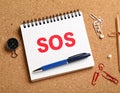 Note with word SOS and stationery on cork board, closeup Royalty Free Stock Photo