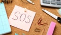Note with word SOS and stationery on cork board, closeup Royalty Free Stock Photo