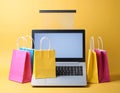 Online shopping. Laptop computer and colored paper bags on a yellow background Royalty Free Stock Photo