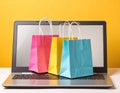 Online shopping. Laptop computer and colored paper bags on a yellow background Royalty Free Stock Photo
