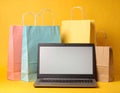 Online shopping. Laptop computer and colored paper bags on a yellow background Royalty Free Stock Photo