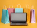 Online shopping. Laptop computer and colored paper bags on a yellow background Royalty Free Stock Photo