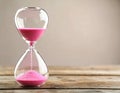 Hourglass with pink flowing sand on wooden table. Space for text Royalty Free Stock Photo