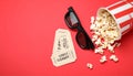 Overturned paper cup with delicious popcorn, cinema tickets and 3D glasses on red bacground Royalty Free Stock Photo