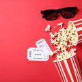 Overturned paper cup with delicious popcorn, cinema tickets and 3D glasses on red bacground Royalty Free Stock Photo