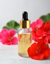 Bottle of geranium essential oil and beautiful flowers on light grey textured table Royalty Free Stock Photo
