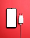 Smartphone and USB charger on red background, flat lay. Modern technology Royalty Free Stock Photo