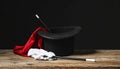 Magician\'s hat, wand and gloves on wooden table against black background Royalty Free Stock Photo
