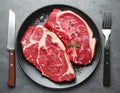 A white plate holds several raw beef steaks, garnished with sprigs of rosemary Royalty Free Stock Photo