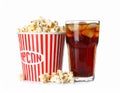 A glass filled with dark soda and ice cubes sits beside a large tub of popcorn. Royalty Free Stock Photo