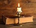 Burning candle in candlestick and old book on wooden table Royalty Free Stock Photo