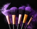 Makeup brushes with purple eye shadow on black background, closeup. Royalty Free Stock Photo