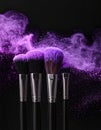 Makeup brushes with purple eye shadow on black background, closeup. Royalty Free Stock Photo