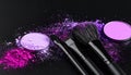 Makeup brushes with purple eye shadow on black background, closeup. Royalty Free Stock Photo