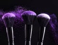 Makeup brushes with purple eye shadow on black background, closeup. Royalty Free Stock Photo