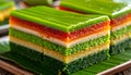 A multicolored layered cake featuring vibrant green, red, and yellow hues, placed on a banana leaf. Royalty Free Stock Photo