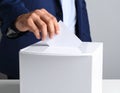 Man putting his vote into ballot box on light grey background, closeup Royalty Free Stock Photo