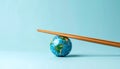 Conceptual image of small globe on light blue background with wooden chopsticks balancing on top Royalty Free Stock Photo