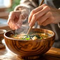 Hands stirring hot miso soup in wooden bowl with rising steam, cozy kitchen Royalty Free Stock Photo