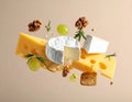 Different types of cheese, crackers, grapes, rosemary and walnuts in air on dark beig Royalty Free Stock Photo