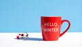 Red mug with words Hello winter on the blue background. Royalty Free Stock Photo