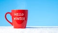 Red mug with words Hello winter on the blue background. Royalty Free Stock Photo