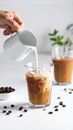 Pouring milk into a glass of iced coffee on a white table, closing Royalty Free Stock Photo