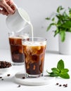 Pouring milk into a glass of iced coffee on a white table, closing Royalty Free Stock Photo