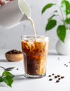 Pouring milk into a glass of iced coffee on a white table, closing Royalty Free Stock Photo