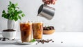 Pouring milk into a glass of iced coffee on a white table, closing Royalty Free Stock Photo