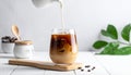 Pouring milk into a glass of iced coffee on a white table, closing Royalty Free Stock Photo