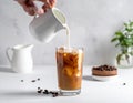 Pouring milk into a glass of iced coffee on a white table, closing Royalty Free Stock Photo