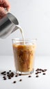 Pouring milk into a glass of iced coffee on a white table, closing Royalty Free Stock Photo