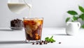 Pouring milk into a glass of iced coffee on a white table, closing Royalty Free Stock Photo