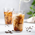 Pouring milk into a glass of iced coffee on a white table, closing Royalty Free Stock Photo