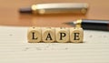 Wooden Blocks Spelling \'LAPE\' on Lined Paper with Pen Royalty Free Stock Photo