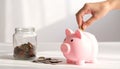 Hand Inserting Coin into Pink Piggy Bank Next to Jar of Coins Royalty Free Stock Photo