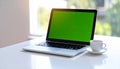 Laptop with green screen on desk, coffee cup nearby, natural light, workspace Royalty Free Stock Photo