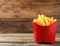 Delicious french fries in paper box on wooden table, space for text Royalty Free Stock Photo