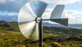 Small Wind Vane Spinning in a Hilly Landscape with Distant Wind Turbine Royalty Free Stock Photo
