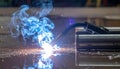 Welding metal with sparks and blue smoke in a factory. Industrial metalworking and steel fabrication process close-up. Royalty Free Stock Photo