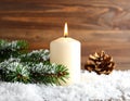 Fir branch in snow, lighted candle, cone on wooden background. Christmas theme Royalty Free Stock Photo