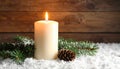 Fir branch in snow, lighted candle, cone on wooden background. Christmas theme Royalty Free Stock Photo