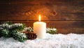 Fir branch in snow, lighted candle, cone on wooden background. Christmas theme Royalty Free Stock Photo