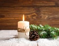 Fir branch in snow, lighted candle, cone on wooden background. Christmas theme Royalty Free Stock Photo