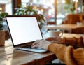 woman working on a laptop with a blank white screen in a cozy cafe with coffee and plants Royalty Free Stock Photo