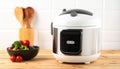 Electric rice cooker with a stainless steel body and white top, featuring a digital control panel, sits on a wooden countertop. Royalty Free Stock Photo