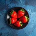 Fresh strawberries on a small black plate against a blue plaster design board. Royalty Free Stock Photo