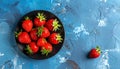 Fresh strawberries on a small black plate against a blue plaster design board. Royalty Free Stock Photo