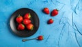 Fresh strawberries on a small black plate against a blue plaster design board. Royalty Free Stock Photo